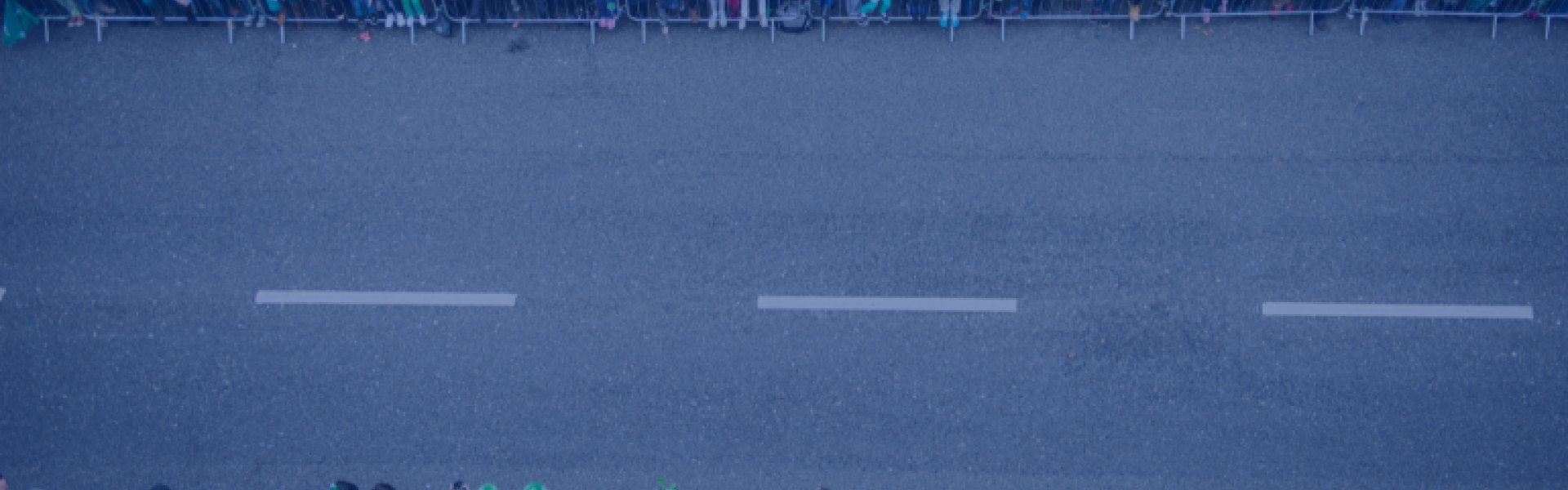 A road prepared for a parade. People gathered either side behind barriers wearing Irish themed paraphernalia 