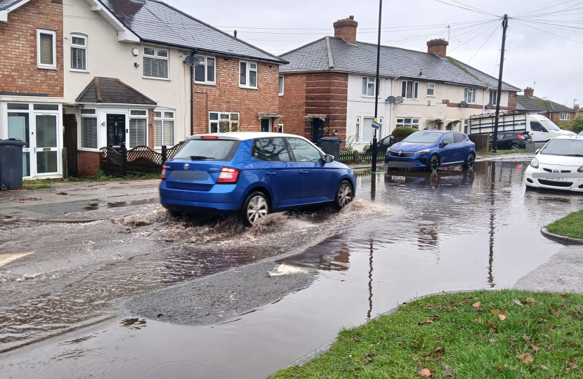 Flooded road with cars driving, causing a small wave