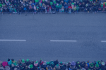 A road prepared for a parade. People gathered either side behind barriers wearing Irish themed paraphernalia 