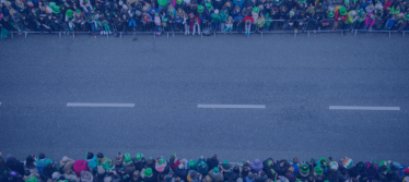 A road prepared for a parade. People gathered either side behind barriers wearing Irish themed paraphernalia 